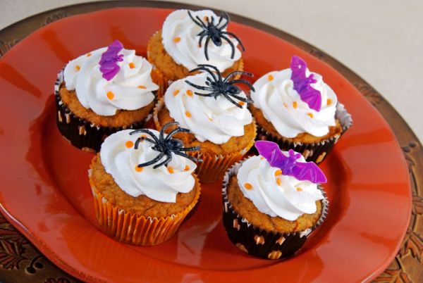 Pumpkin spice cupcakes with vanilla icing decorated with spiders and bats.